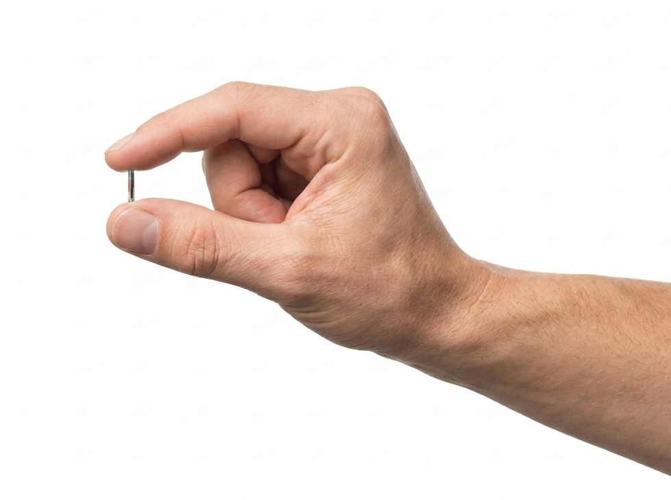 A hand holding the SkinID implant between two fingers, showing its actual size